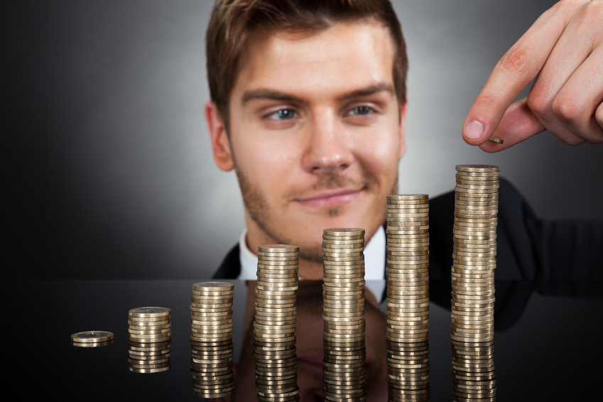 Young Businessman Stacking Coins At Desk